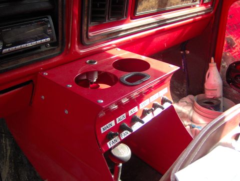 1978 Ford Bronco - Interior shot of a vehicle's dashboard, focusing on a red custom console with auxiliary switches and cup holders.