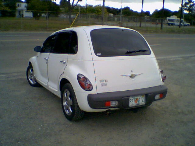 White PT Cruiser, rear three-quarter view, chrome wheels, on a gravel lot