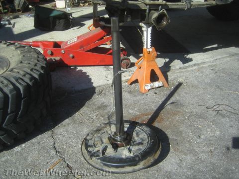 1987 Suzuki Samurai - A detached rear axle assembly is supported by jack stands, with a large tire and a red floor jack visible nearby.