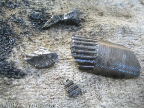 1987 Suzuki Samurai - Several pieces of a broken metal gear with visible teeth are scattered on a textured cloth surface.