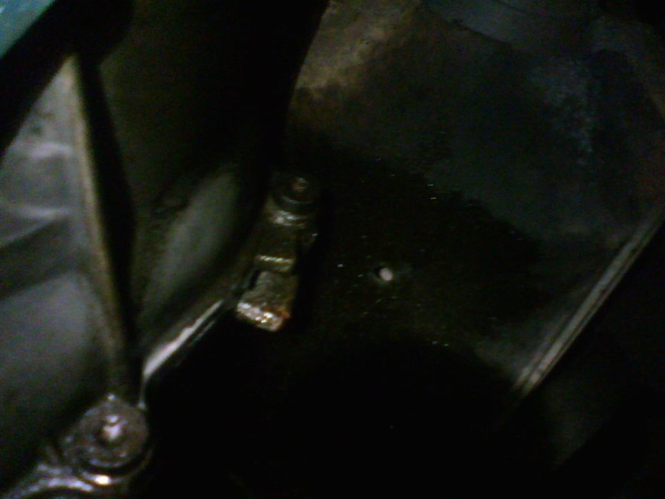 Dark close-up of an oily engine or transmission bracket area