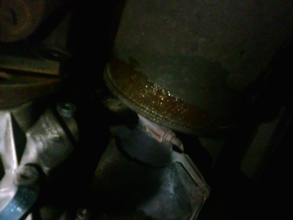 Dark close-up of a rusty engine component with oil residue