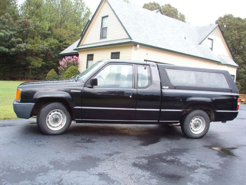 1993 Mitsubishi FTO - A black pickup truck with a camper shell is parked in front of a house.