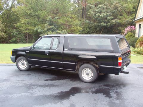 1993 Mitsubishi FTO - Side view of a black pickup truck with a camper shell, parked outdoors.