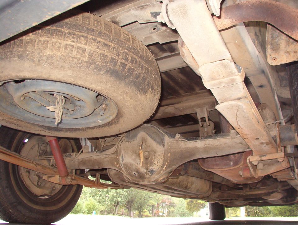 Underside view of a vehicle showing the spare tire, leaf springs, and differential. There's a watermark for Supermotors.net