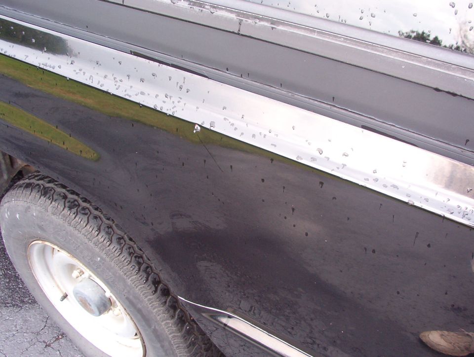 Wet dark car body side with chrome trim, chips, and white steel wheel