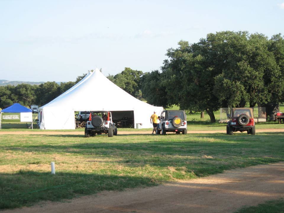 Three Jeep Wranglers parked on grass near a large white tent. One person stands by a white Jeep