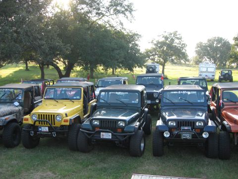 2001 Jeep Wrangler - A group of Jeep Wranglers are parked on a grassy area with trees and RVs in the distance.