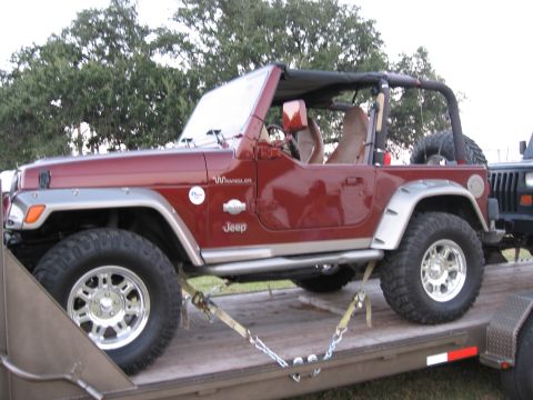 2001 Jeep Wrangler - A red Jeep Wrangler is secured to a trailer with straps and chains, ready for transport.