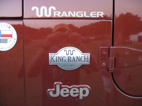 2001 Jeep Wrangler - Close-up of a red Jeep Wrangler's side panel, showing various emblems and the vehicle's door hinge.