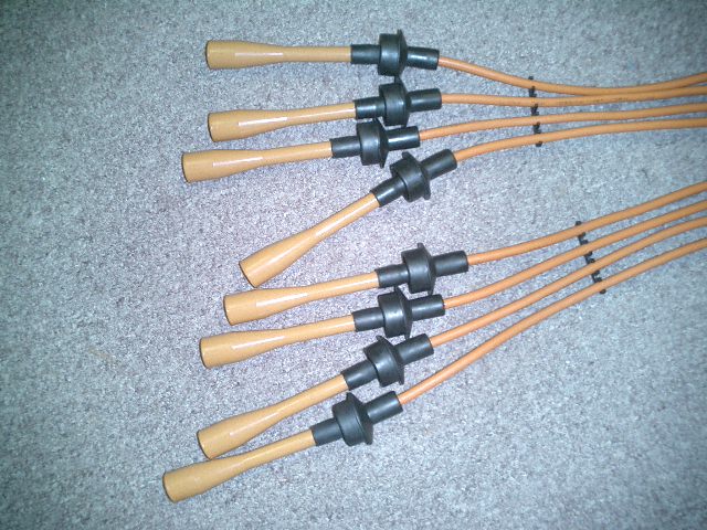 Set of orange spark plug wires with tan boots and black connectors, laid out on a carpeted surface