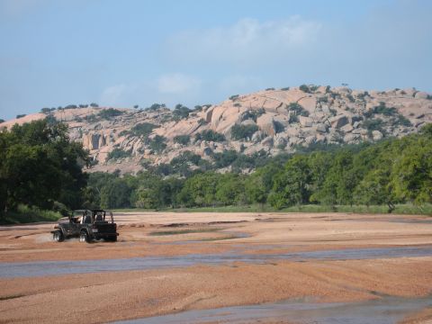 2001 Jeep Wrangler - A black Jeep Wrangler navigates a sandy riverbed with a large, boulder-strewn hill under a clear blue sky.