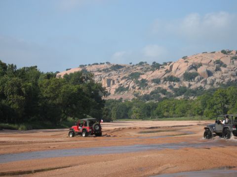 2001 Jeep Wrangler - Two Jeep Wranglers navigate a sandy, watery terrain with a large, rocky hill formation in the distance.