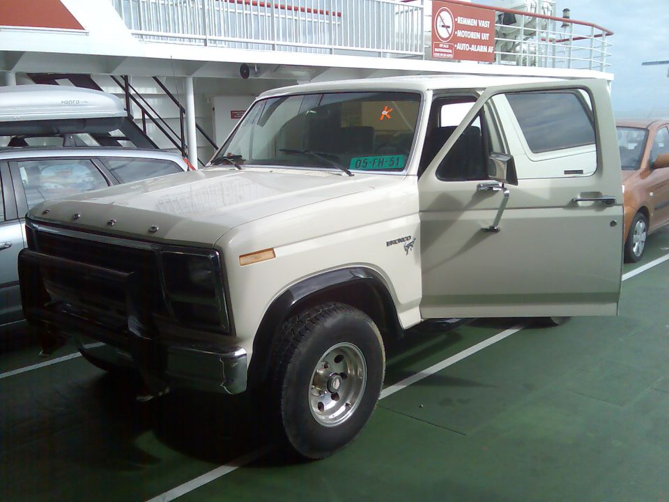 Cream-colored Ford Bronco with driver's door open, parked on a ferry deck