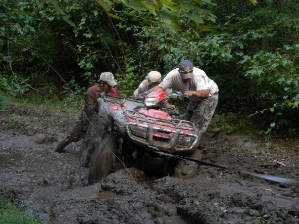 Red ATV stuck in deep mud, with three people trying to free it
