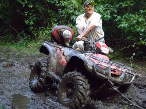 1992 Ford F-150 - Two individuals struggle with a muddy ATV in a wooded area.