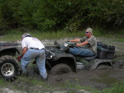 1992 Ford F-150 - Two ATVs are stuck deep in the mud, with one rider waiting and another attempting to help.