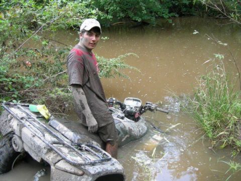 1992 Ford F-150 - A person covered in mud stands next to a muddy ATV submerged in water.