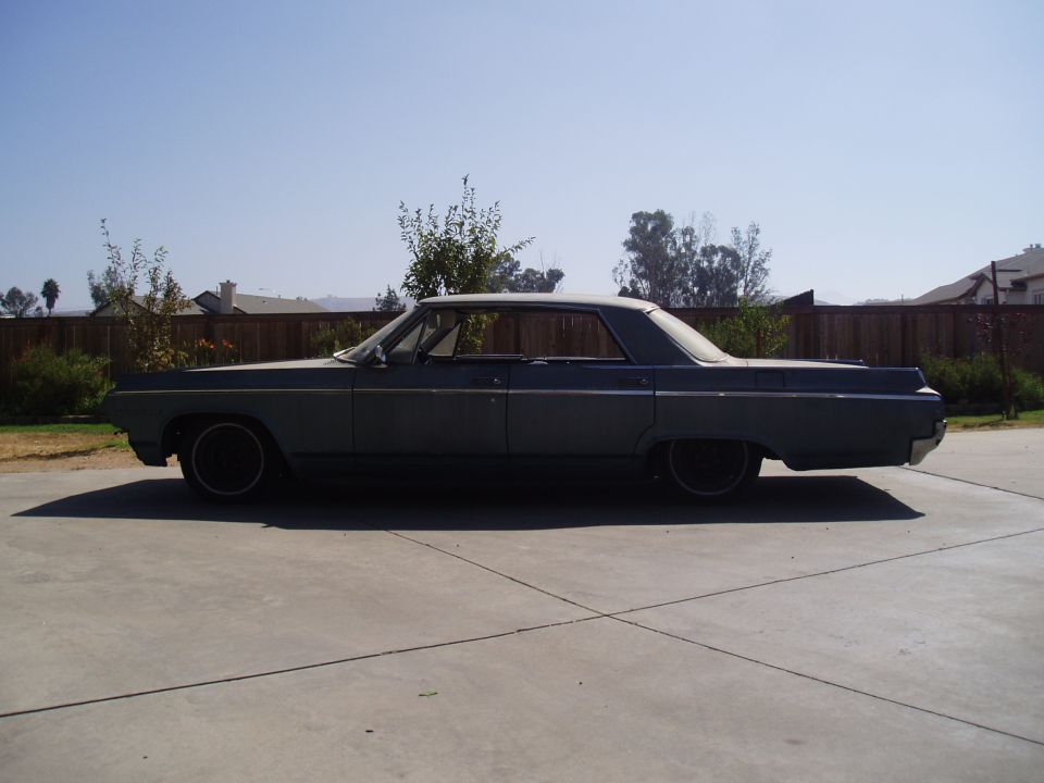 Side view of dark 1960s two-door hardtop with white roof, lowered on black wheels