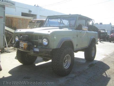 1990 Ford Bronco - light blue first-generation Ford Bronco with a lift and mud tires sits outside a repair shop.