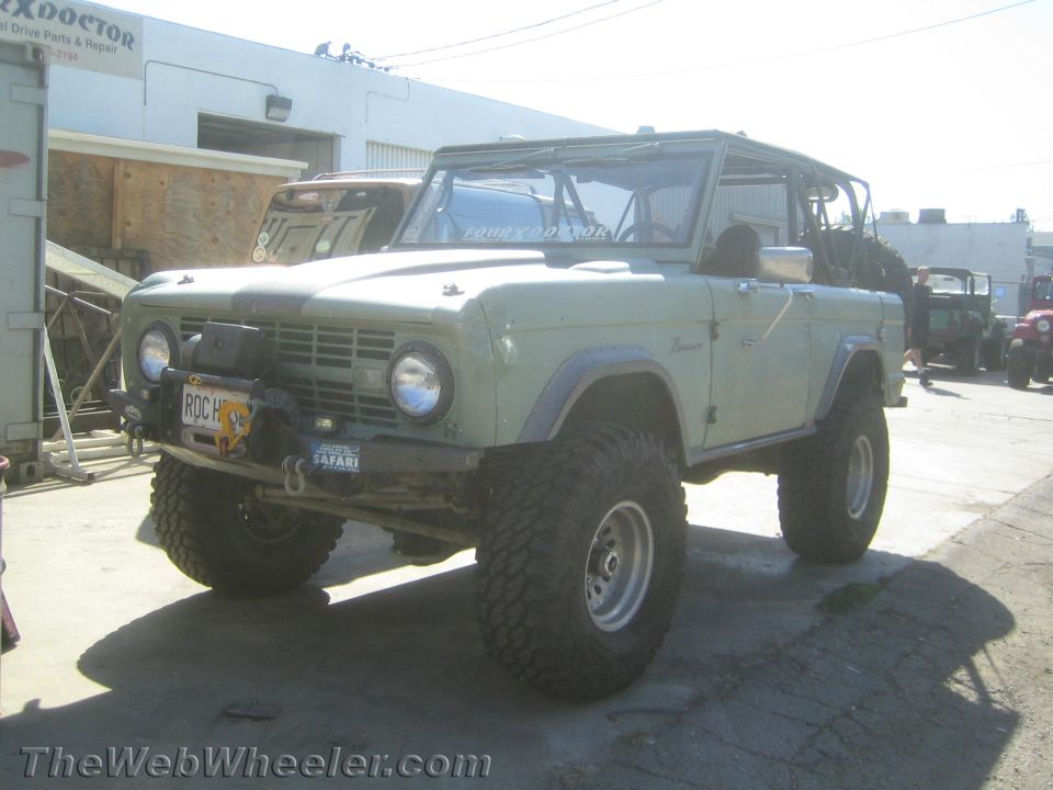 Light blue early Ford Bronco with lift kit parked at a shop