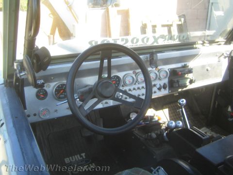 1990 Ford Bronco - stripped interior of an off-road vehicle showing a small steering wheel, a row of aftermarket gauges and floor shifters.