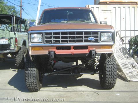 1990 Ford Bronco - Front view of a brown lifted Ford Bronco II showing its chrome grille, solid front axle and large off-road tires.