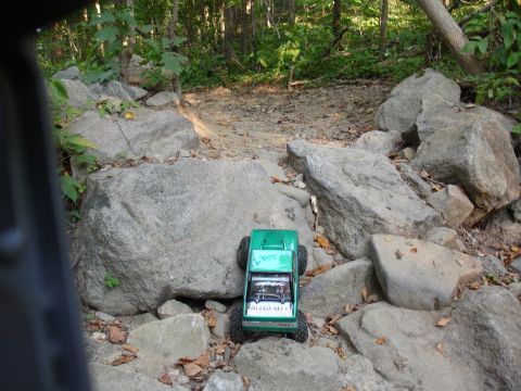 1996 Ford Bronco - A remote-controlled rock crawler navigates a challenging, boulder-strewn path in a wooded area.