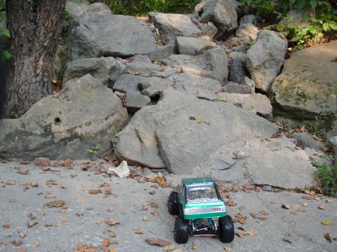 1996 Ford Bronco - A green remote-controlled truck with "FORD" visible on its grille sits on a concrete surface near a pile of large rocks.