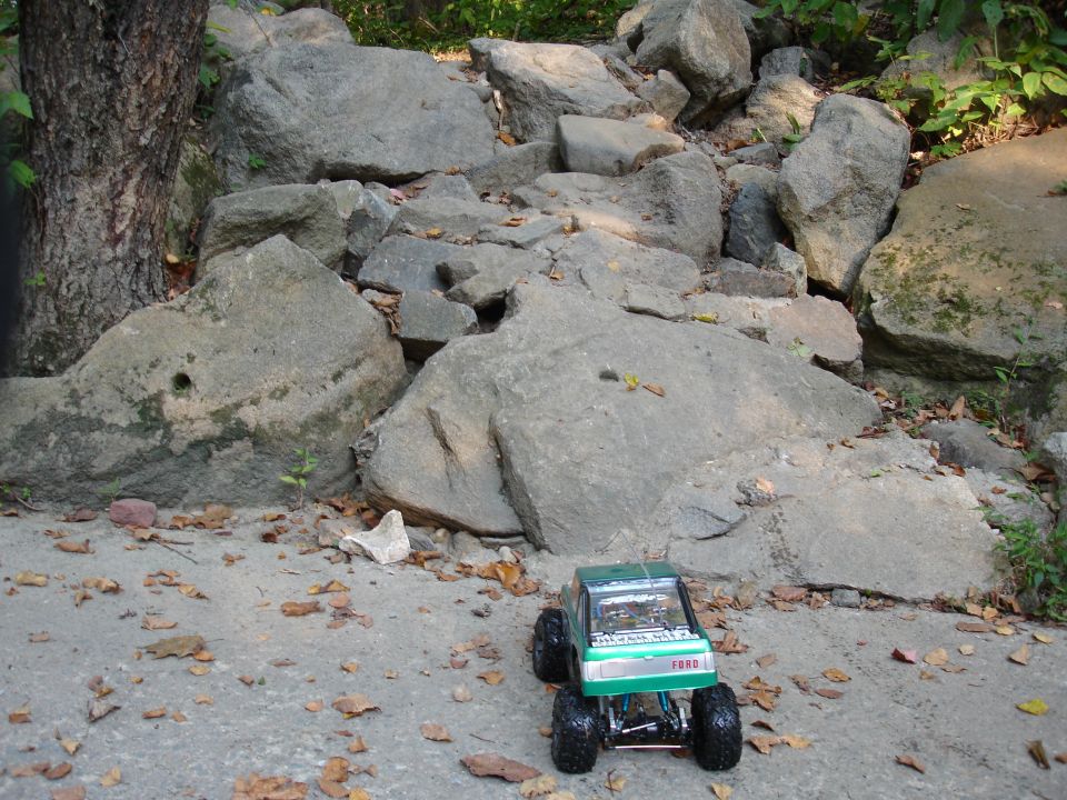 Green RC truck with "FORD" on grille, parked on concrete near rocks