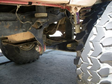1995 Ford Bronco - Close-up view of the undercarriage and suspension of a red vehicle, focusing on the tire and frame.