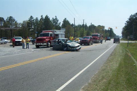 1998 Ford Crown Victoria - A severely damaged 1998 Ford Crown Victoria sits at an intersection following a collision, with emergency services on the scene.