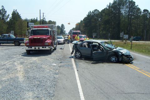 1998 Ford Crown Victoria - Emergency responders are present at the scene of a car accident involving a heavily damaged sedan.