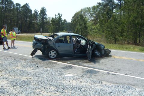 1998 Ford Crown Victoria - A severely damaged sedan sits on the shoulder of a road, with emergency personnel observing the scene.