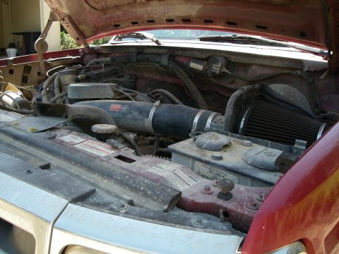 1995 Ford Bronco - The engine bay of a red 1995 Ford Bronco, an aftermarket air filter and visible hoses and components.