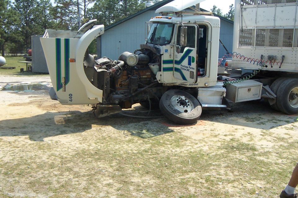 Semi-truck with hood open and front end damage, parked outdoors. A trailer is attached