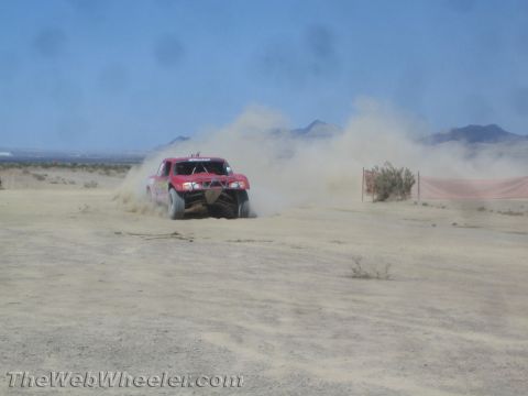 1990 Ford Bronco - red off-road race truck corners hard, throwing up a heavy cloud of dust in the desert.