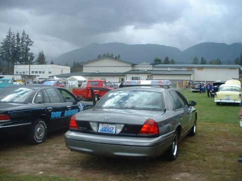 2000 Ford Crown Victoria - A gray police car, likely a 2000 Ford Crown Victoria, is parked at an outdoor event with other vehicles.