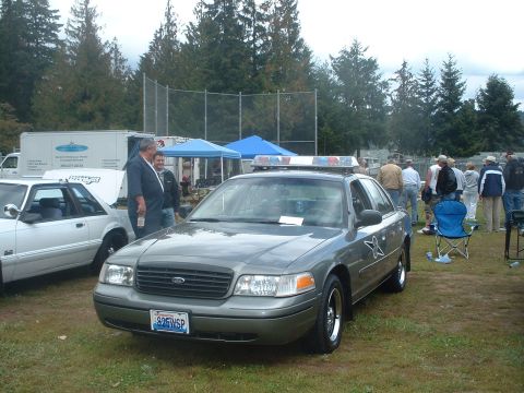 2000 Ford Crown Victoria - Police car with light bar and a star emblem on the door, parked at an outdoor event.