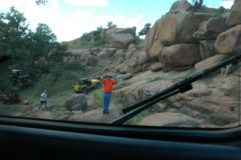 2001 Jeep Wrangler - Multiple Jeep Wranglers navigate a challenging off-road course amidst large rock formations and sparse vegetation.