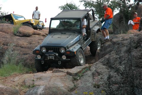 2001 Jeep Wrangler - A black Jeep Wrangler tackles a challenging rocky trail, with a yellow Jeep visible in the background.