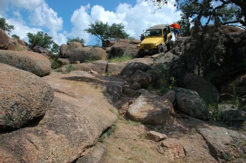 2001 Jeep Wrangler - A yellow 2001 Jeep Wrangler navigates a challenging rocky terrain, with another vehicle visible in the distance.
