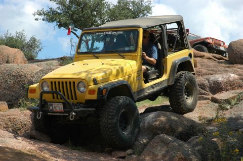 2001 Jeep Wrangler - A yellow Jeep Wrangler navigates a rocky terrain, with another Jeep visible in the background.