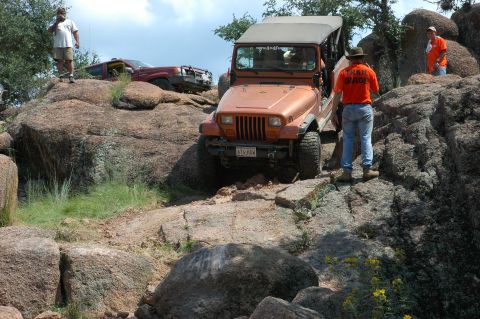 2001 Jeep Wrangler - An orange Jeep Wrangler navigates a challenging rocky trail with a trail guide observing.