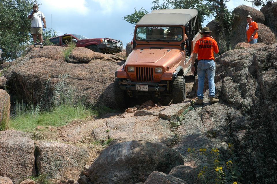 Orange Jeep Wrangler on rocky terrain, front view, soft top up, license plate visible