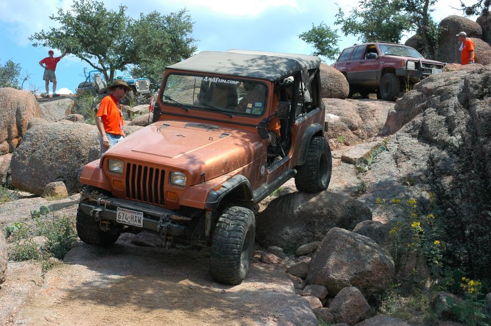 Orange Jeep Wrangler navigating rocky terrain, red Jeep Grand Cherokee in background