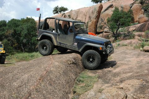 2001 Jeep Wrangler - A dark blue Jeep Wrangler navigates a rocky incline, with another Jeep partially visible in the background.