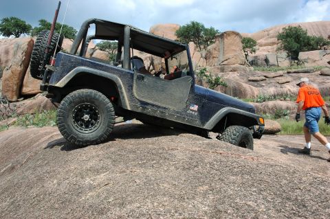 2001 Jeep Wrangler - A dark blue Jeep Wrangler navigates a challenging rocky trail, with a trail guide observing.