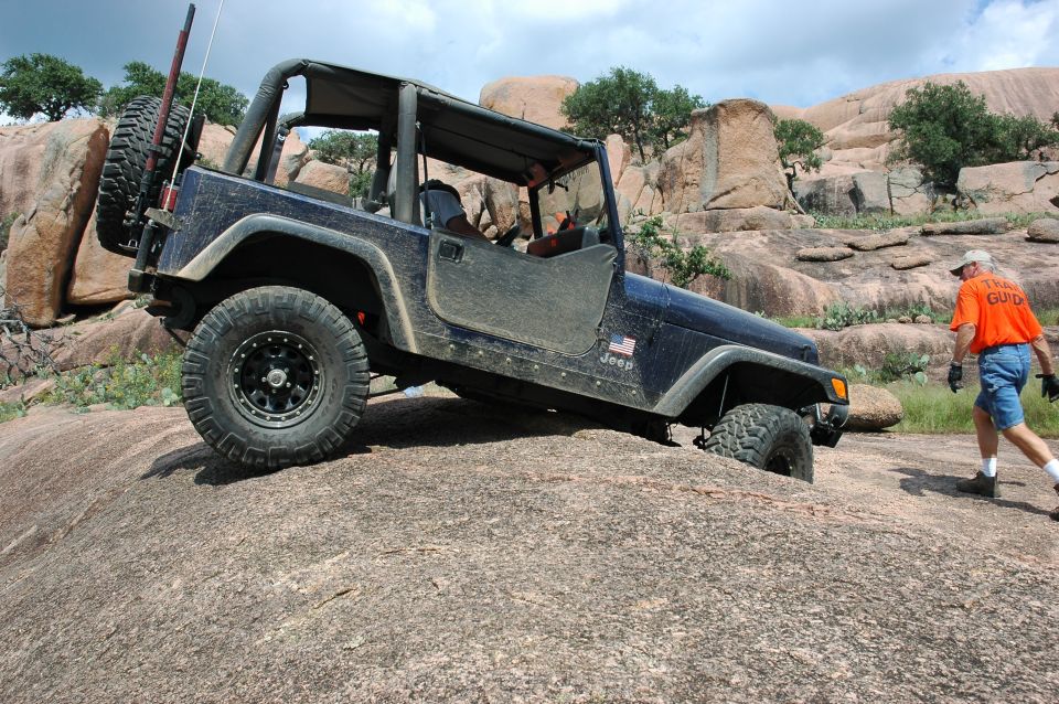 Dark blue Jeep Wrangler, lifted with off-road tires, climbing a large rock formation