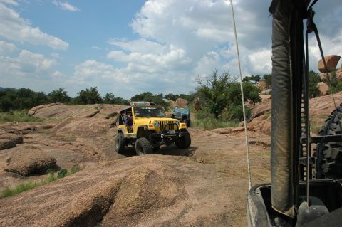 2001 Jeep Wrangler - A yellow 2001 Jeep Wrangler navigates a rocky trail under a cloudy sky, with another vehicle visible in the background.